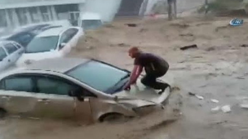 A man holds on to the hood of a car as he is swept away by flood waters ...